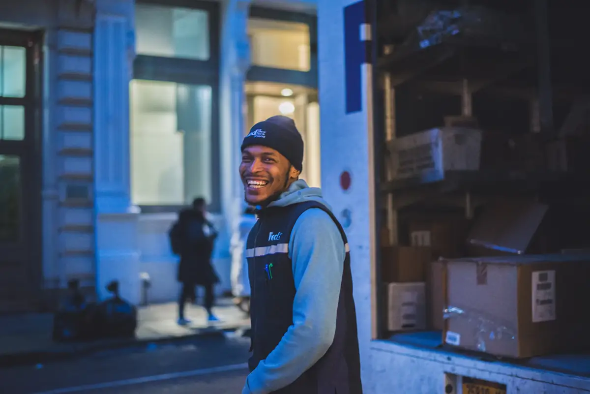 A courier smiling at the door of a delivery van full of parcels