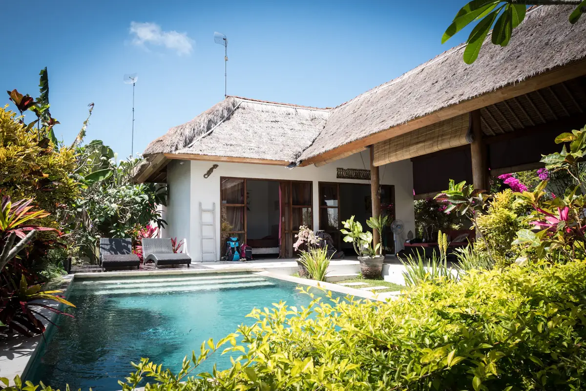 A thatched guest lodge with a pool and a tropical garden