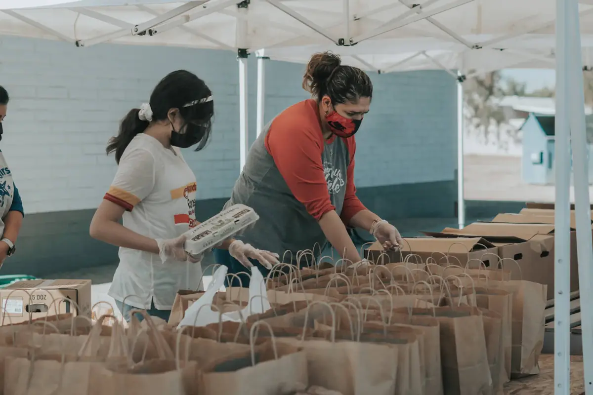 Volunteers packing food parcels into paper bags under a tent