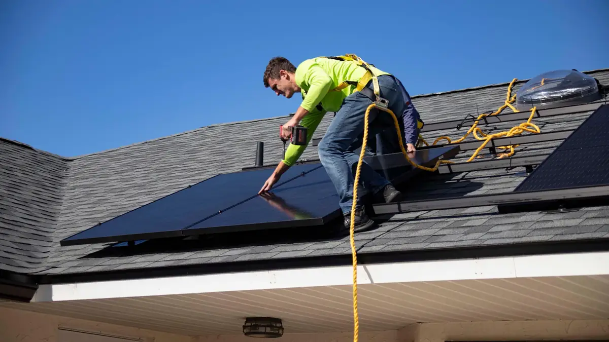 An installer in a harness fitting solar panels on a pitched roof