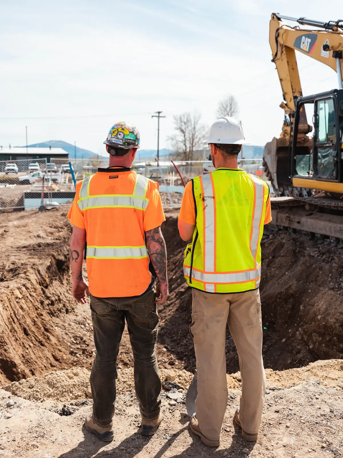Two construction workers in hi-vis vests looking over an excavated site