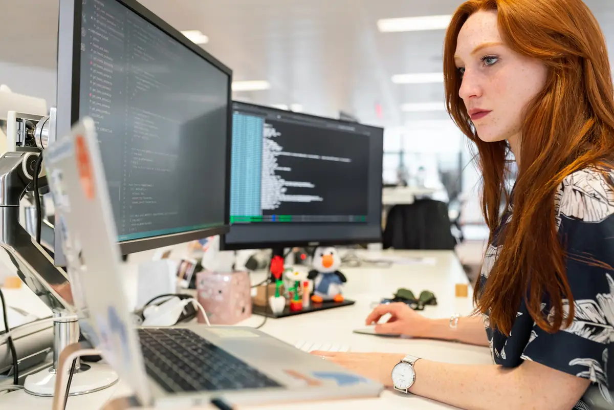 A woman working at two monitors in an open office