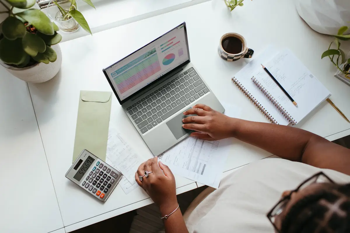 A desk from above: a laptop with a chart, a calculator, a slip and a pen