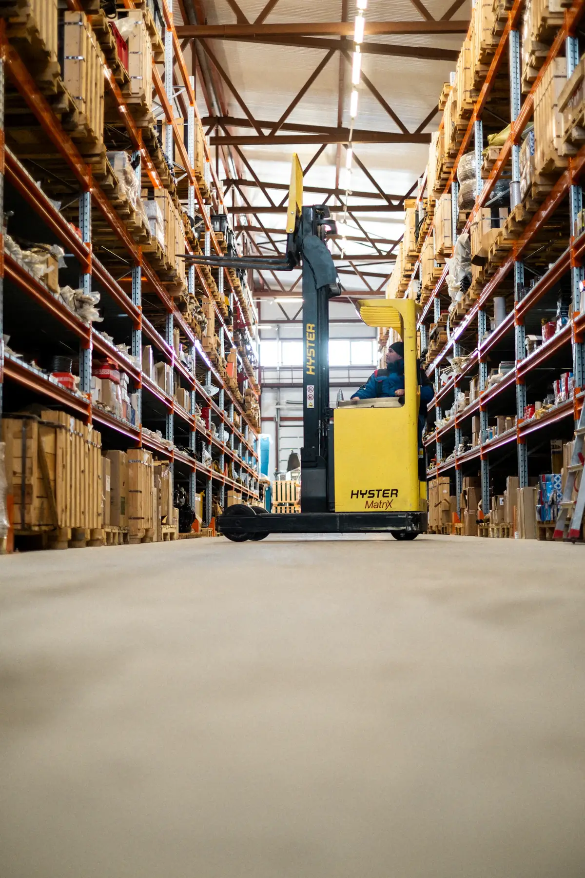 A reach truck between tall racks of stock in a warehouse aisle
