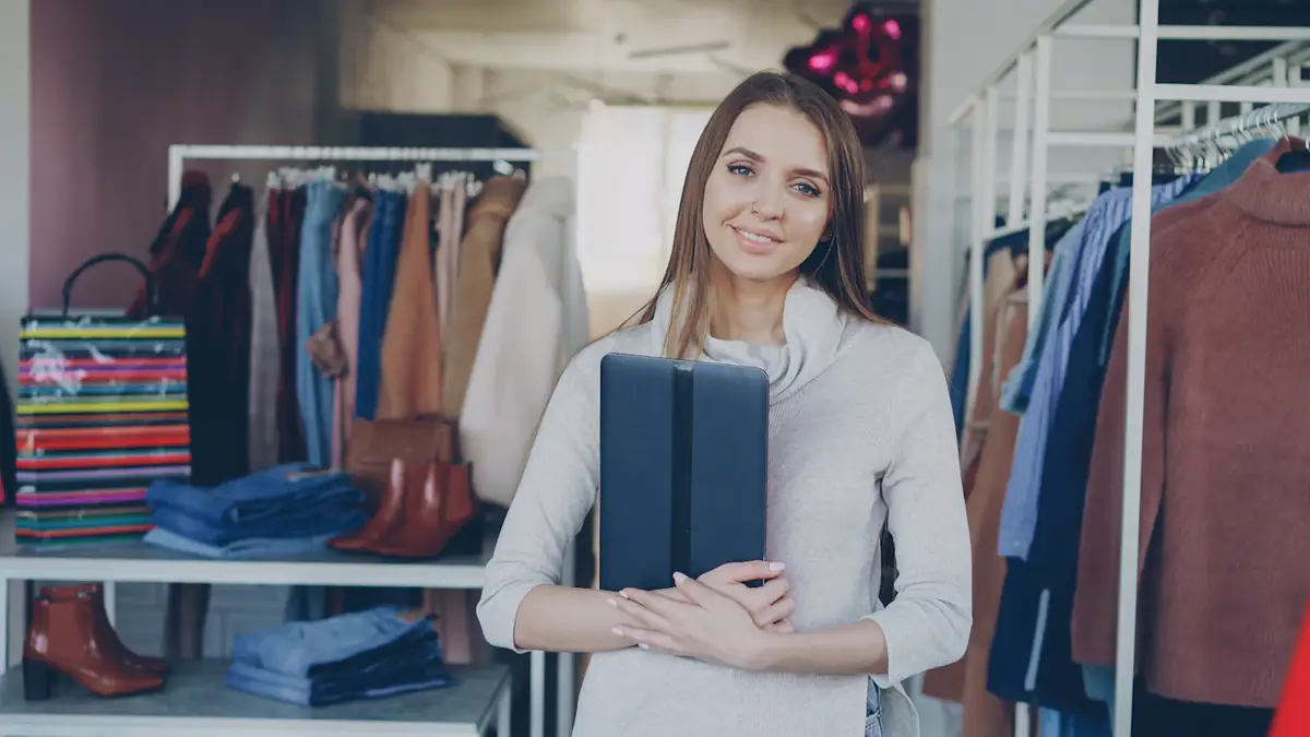 A boutique owner holding a tablet among rails of clothes