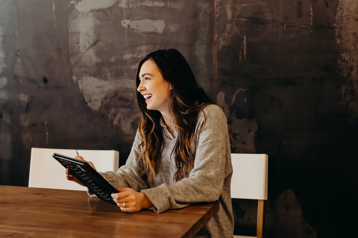 A woman laughing as she works on a tablet at a café table