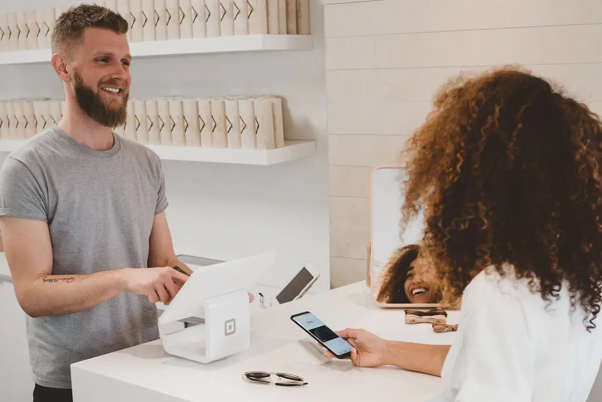 A customer paying by phone at a café counter while the owner smiles