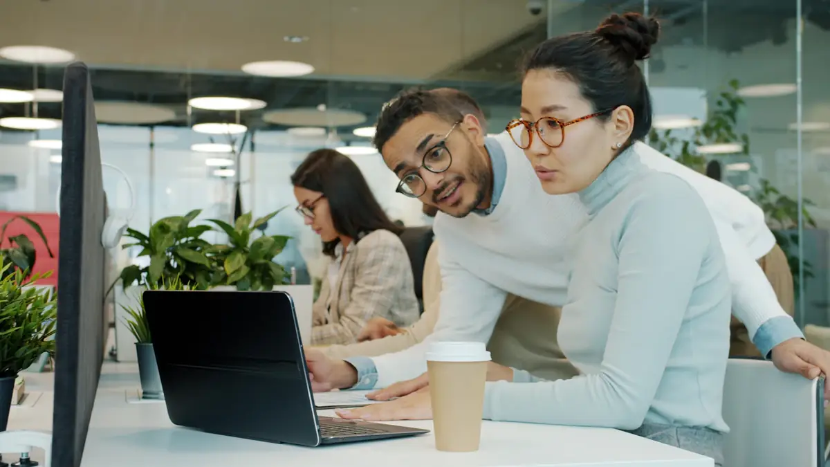 Two people at a laptop working something out together in an open office