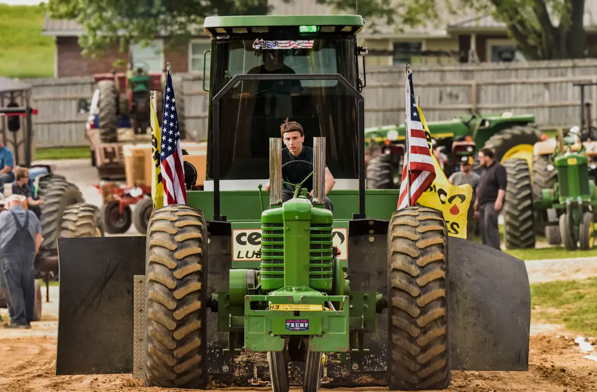 A green tractor at a farm show, flags on either side