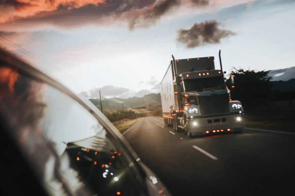 A truck on the highway at dawn, seen in a side mirror