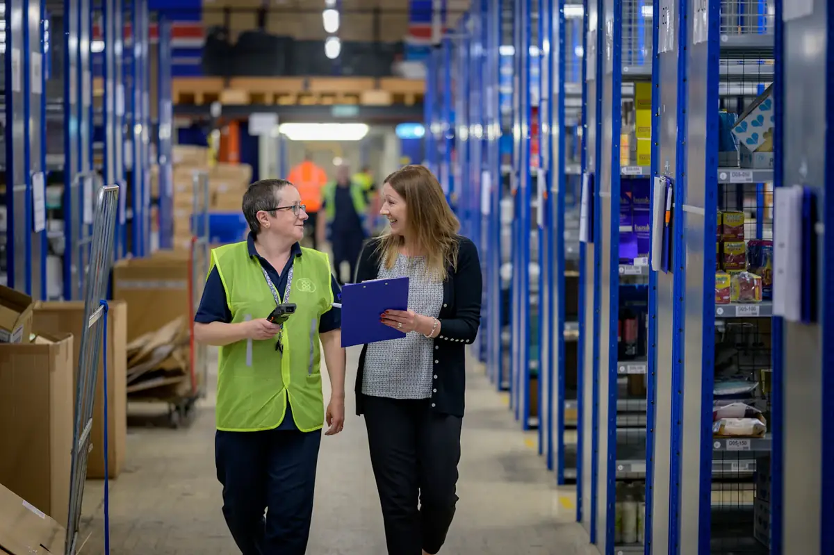 Two warehouse staff walking an aisle, one with a clipboard