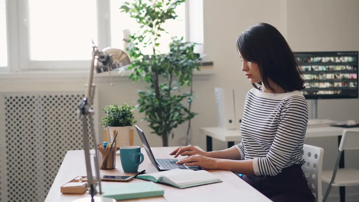 A woman working at her laptop at a desk by a window